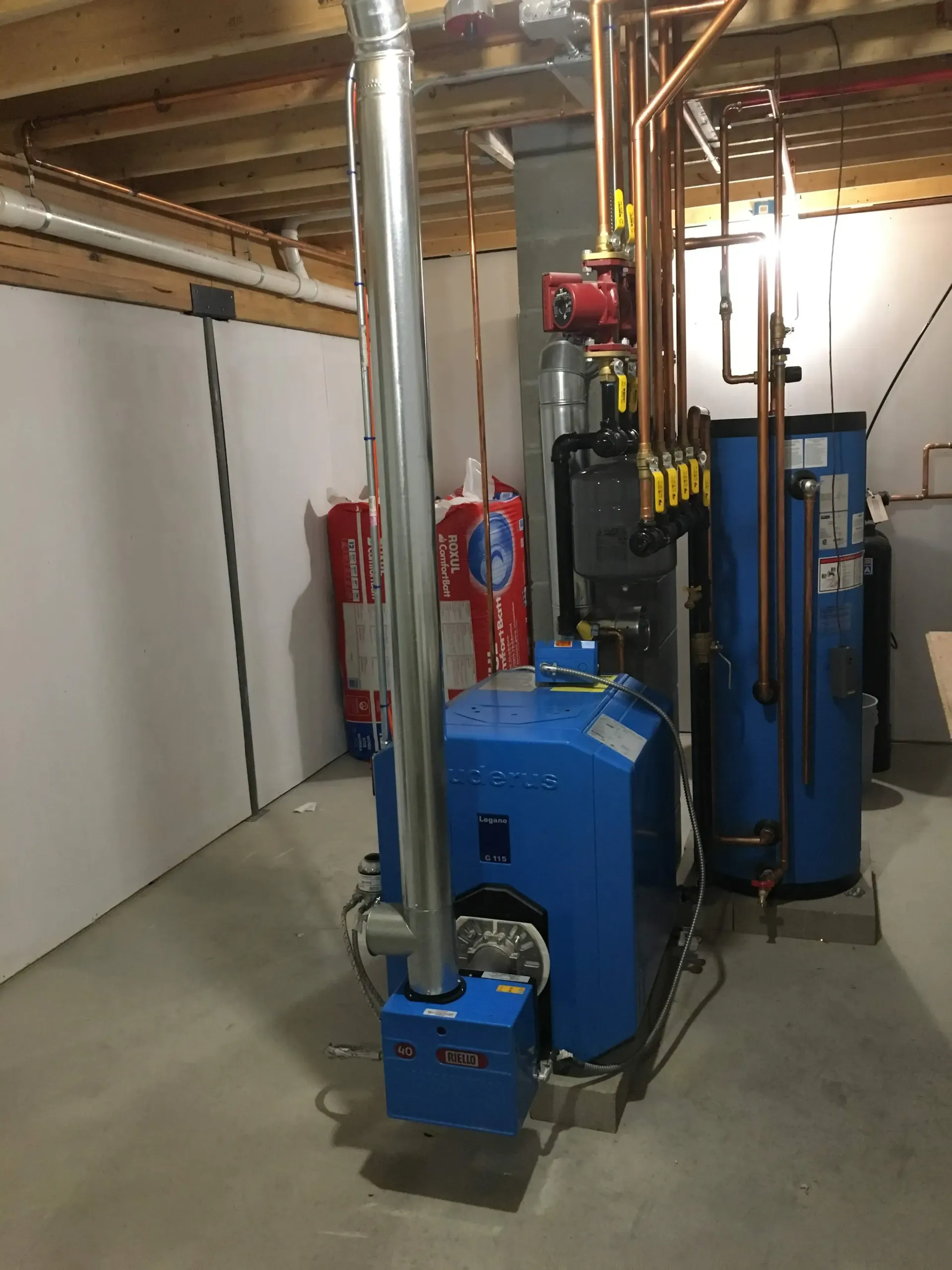 A blue boiler is sitting in a basement surrounded by pipes.