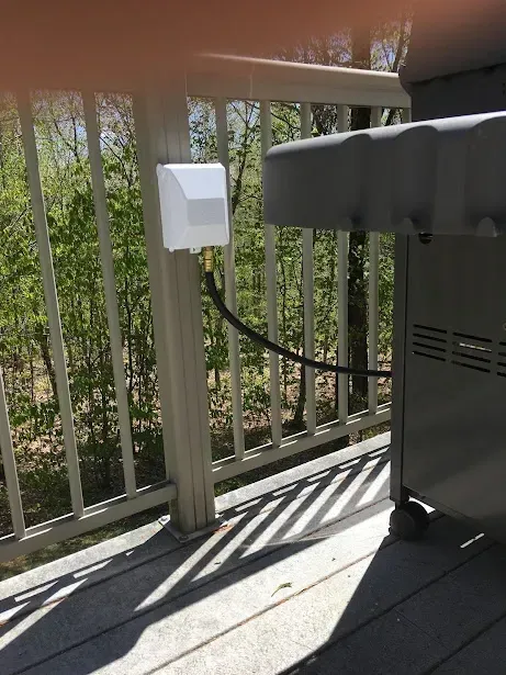 A grill is sitting on a deck next to a railing.