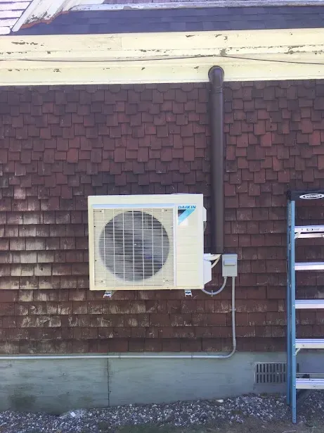 A white air conditioner is mounted on the side of a brick building.