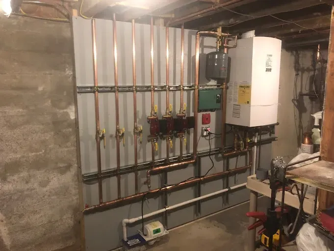 A room with a boiler and pipes hanging on the wall.