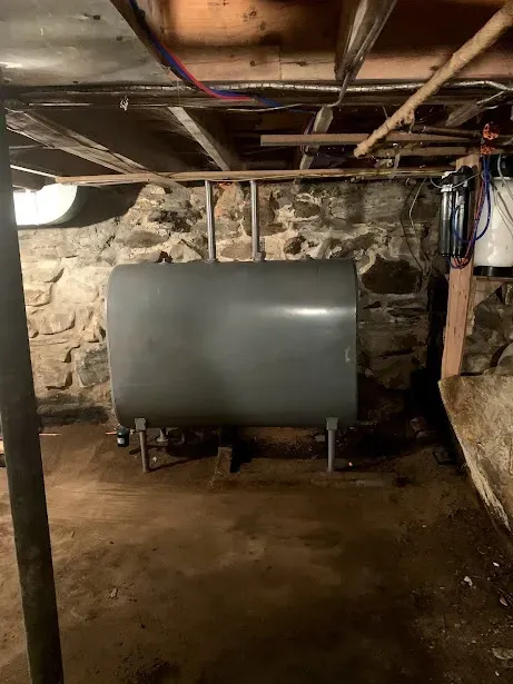 A large metal tank is sitting in a basement next to a stone wall.