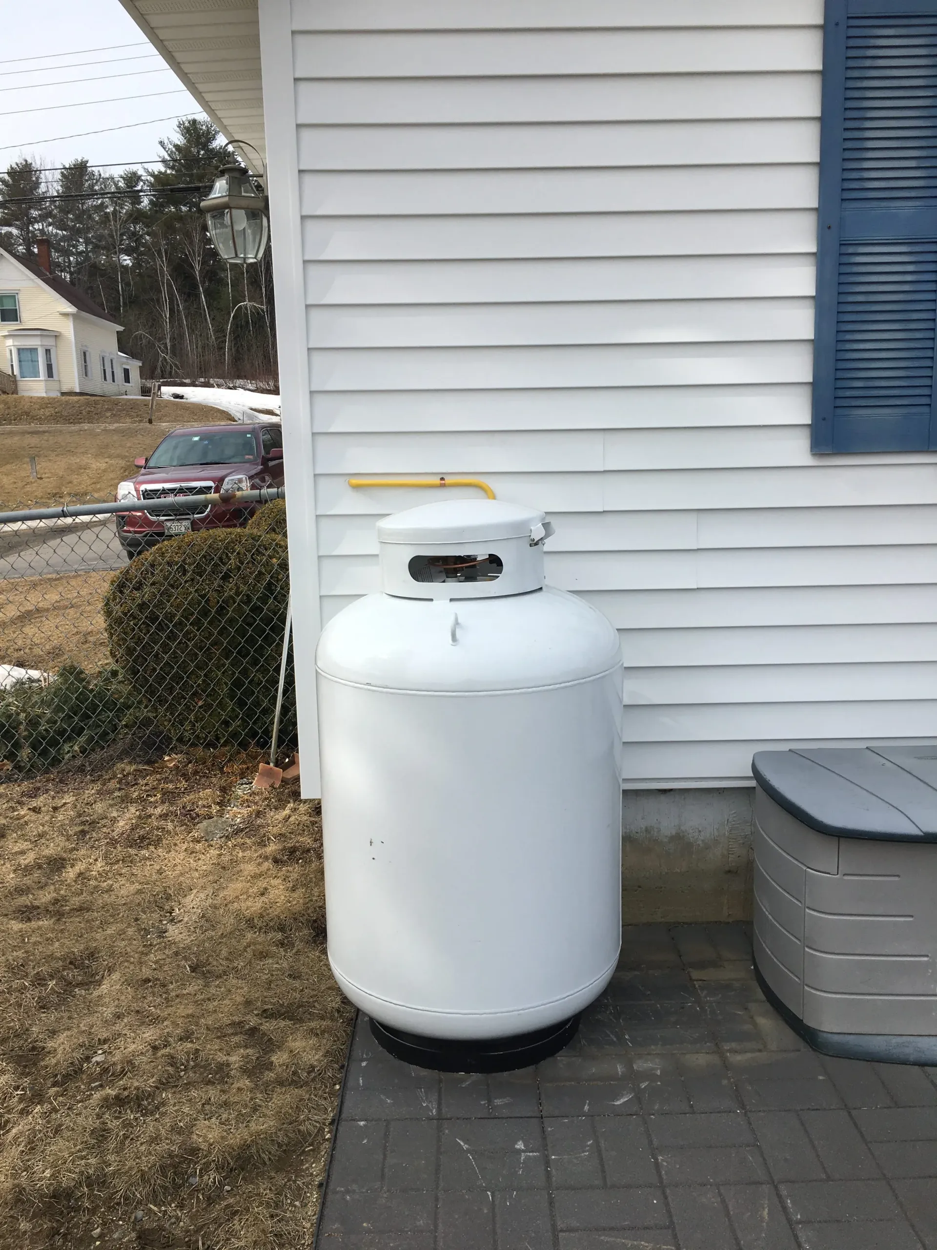 A white propane tank is sitting in front of a white house.