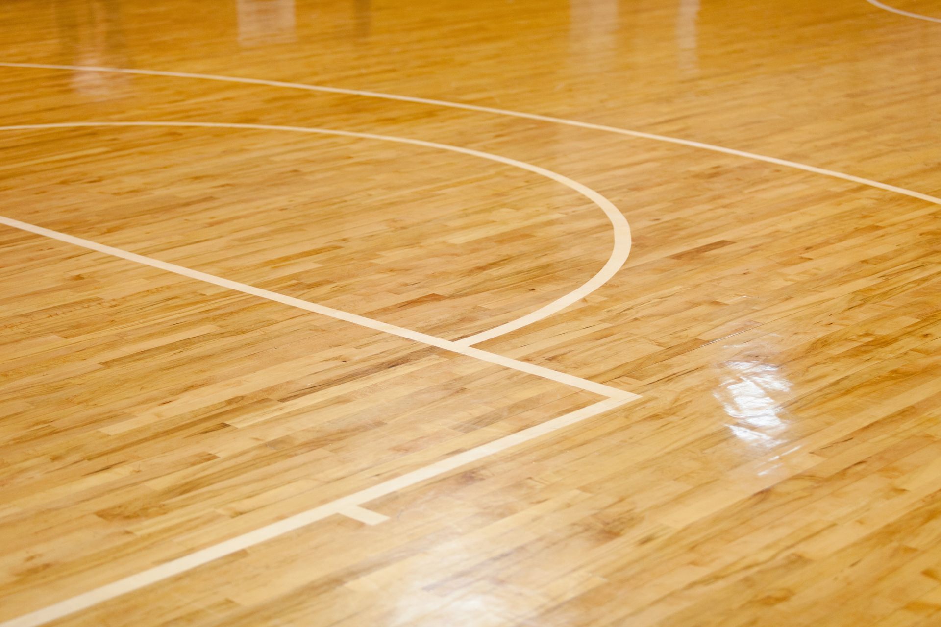 Close-up of a polished wooden basketball court with white boundary lines and a glossy reflection