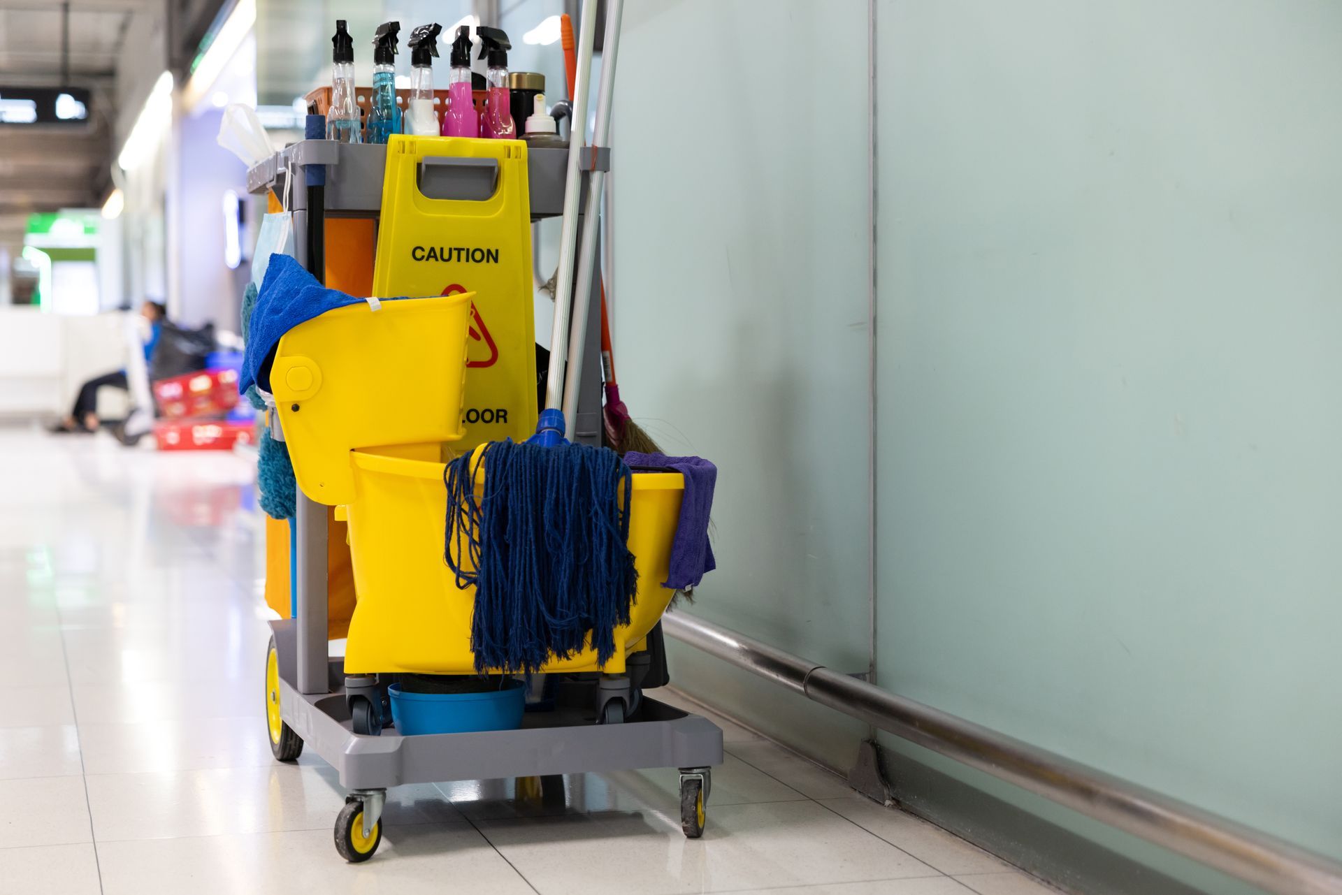 Fully stocked cleaning cart with mop, bucket, and supplies in a building corridor. Fully stocked cleaning cart with mop, bucket, and supplies in a building corridor.