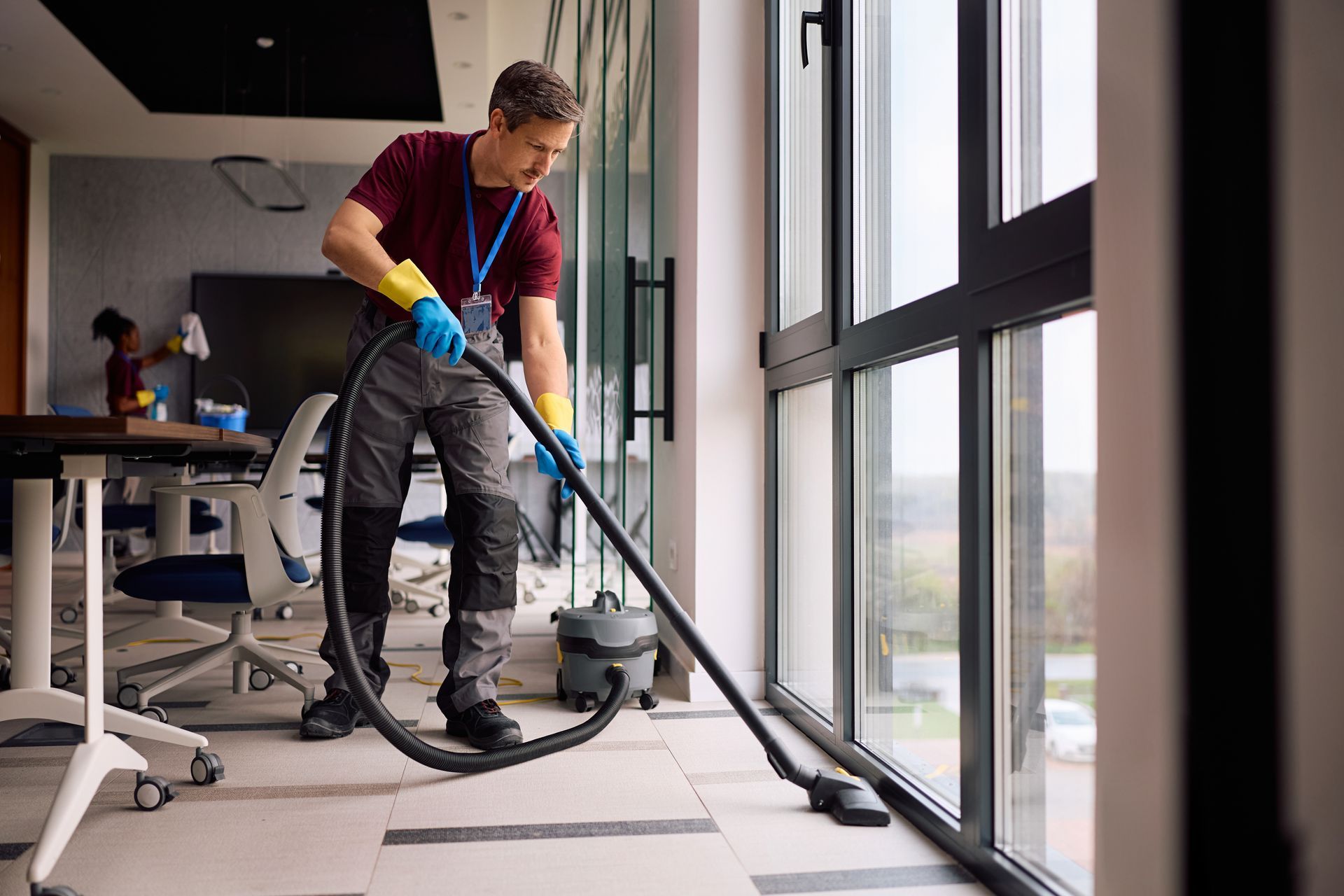 A cleaner is performing office janitorial services, vacuuming floors in a modern office building.