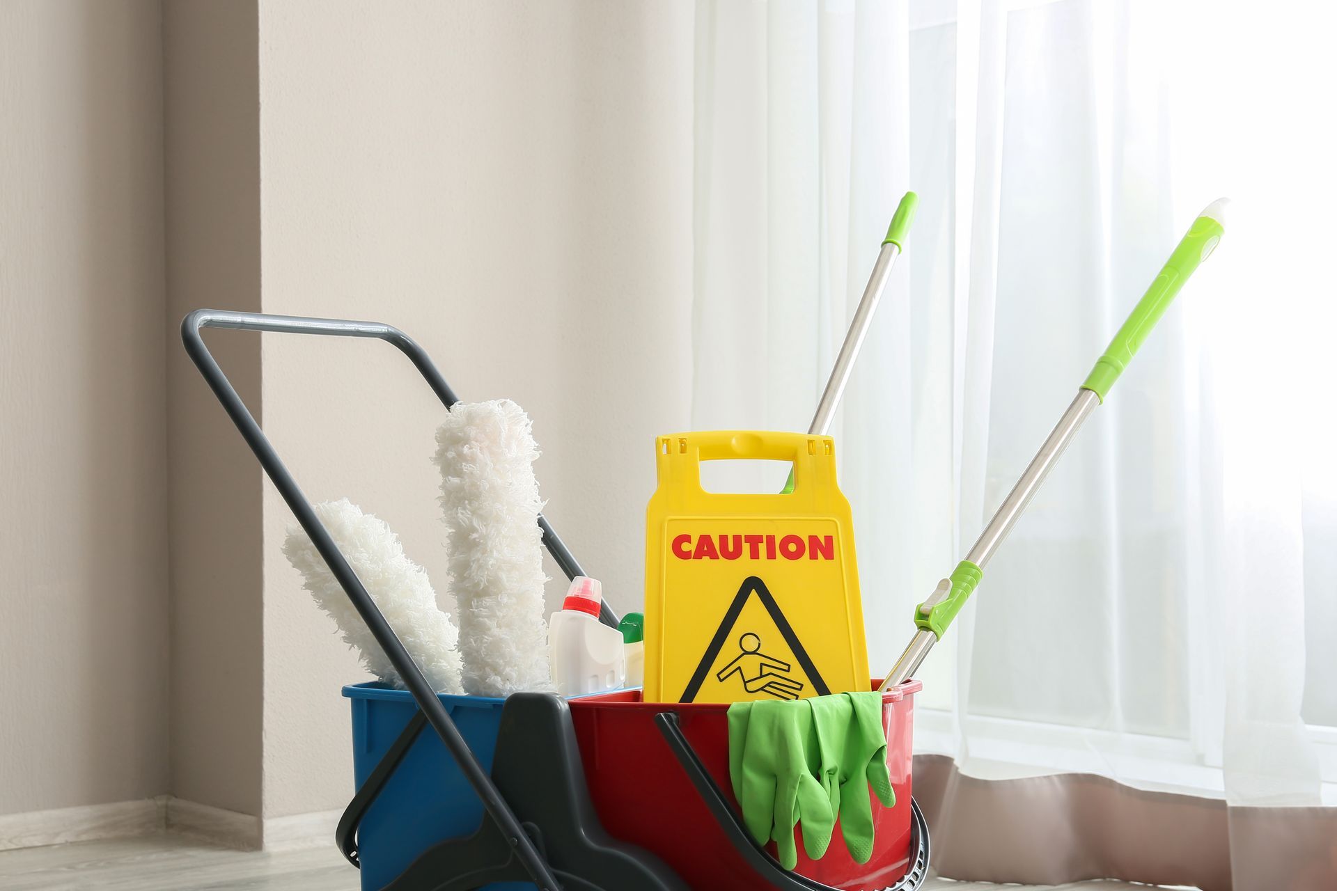Cleaning supplies in a bucket and mop near a window, with a yellow caution sign.