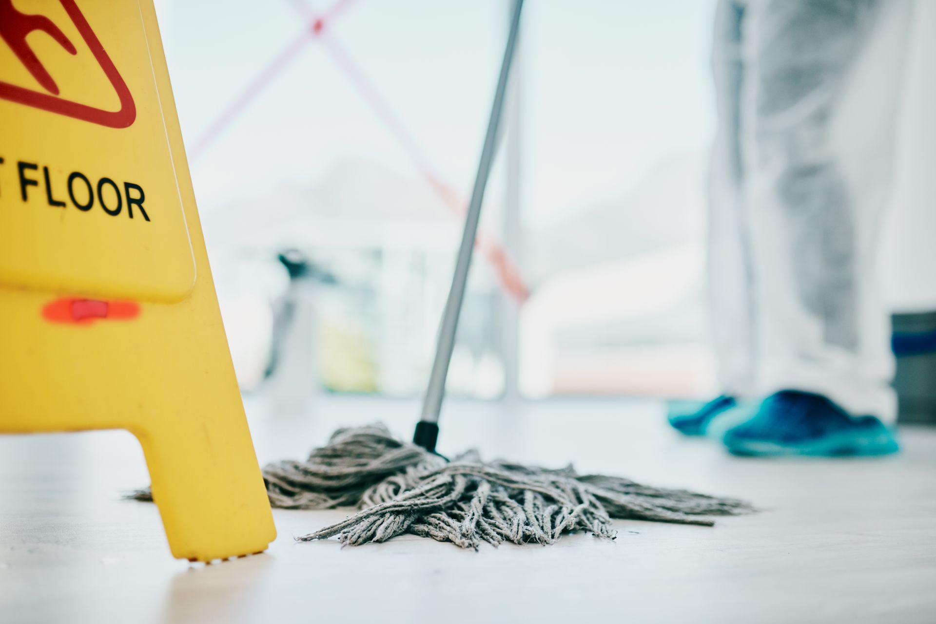 Janitor mopping a clean floor beside a yellow wet floor sign