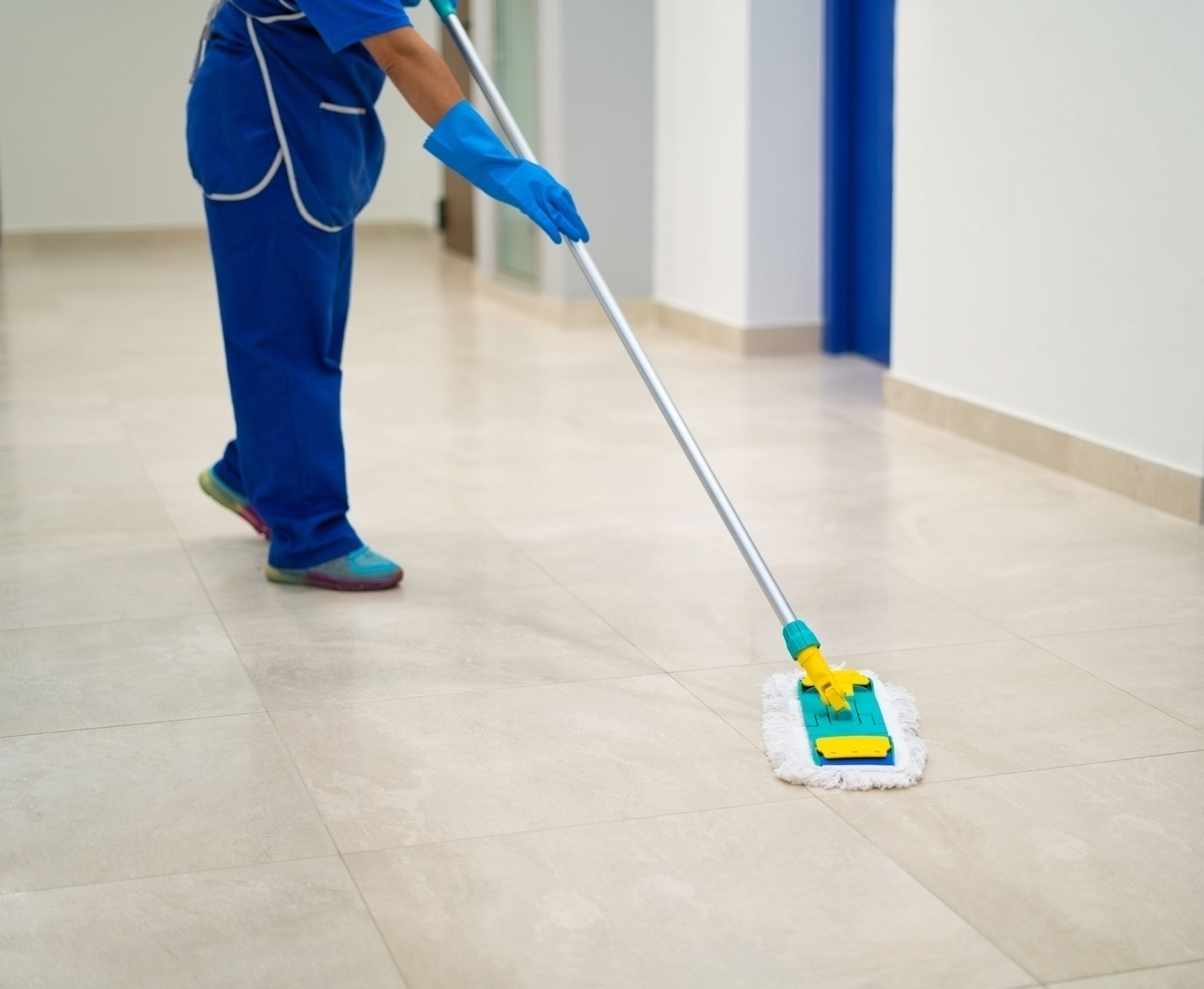 Cleaner mopping a hallway floor with a blue mop and yellow handle