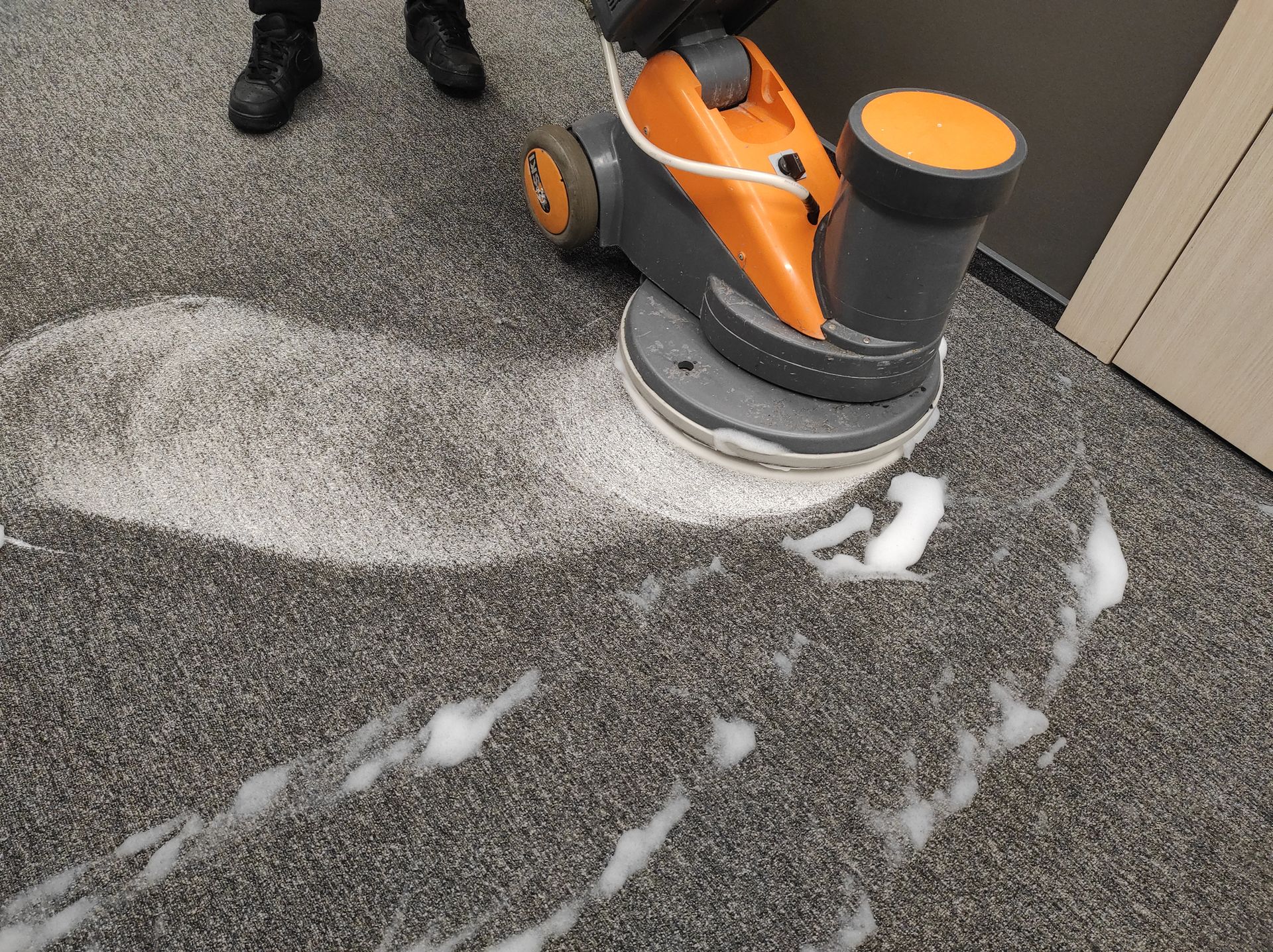 Orange carpet cleaning machine on a gray carpet, with white foam around it.
