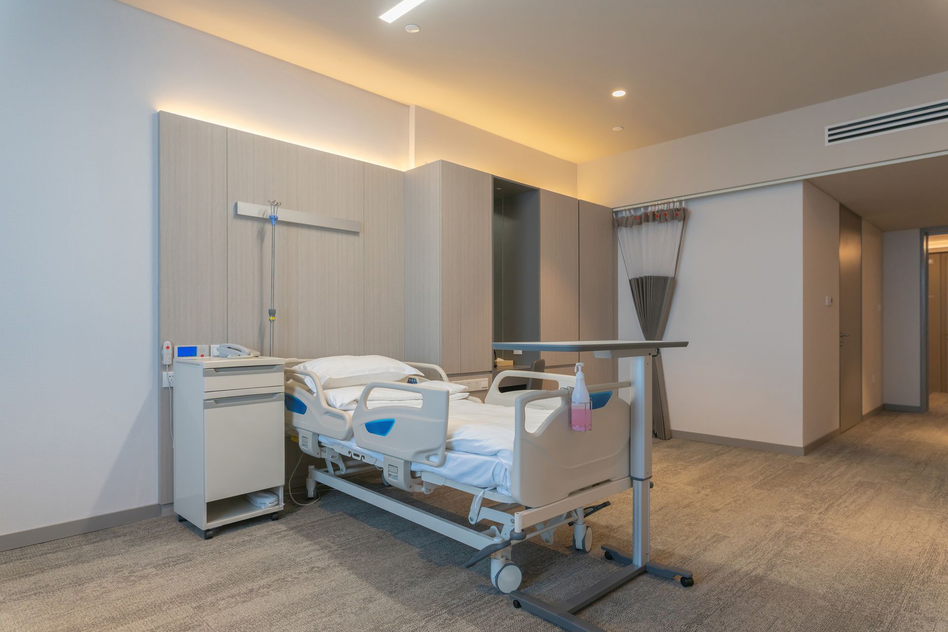 Empty hospital room with adjustable bed, medical equipment, and warm ceiling lighting