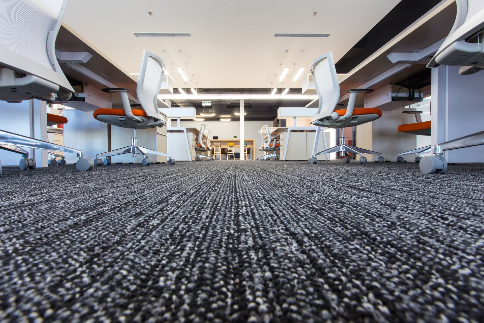 Low-angle view of a modern office with rows of desks and chairs on a patterned carpet.