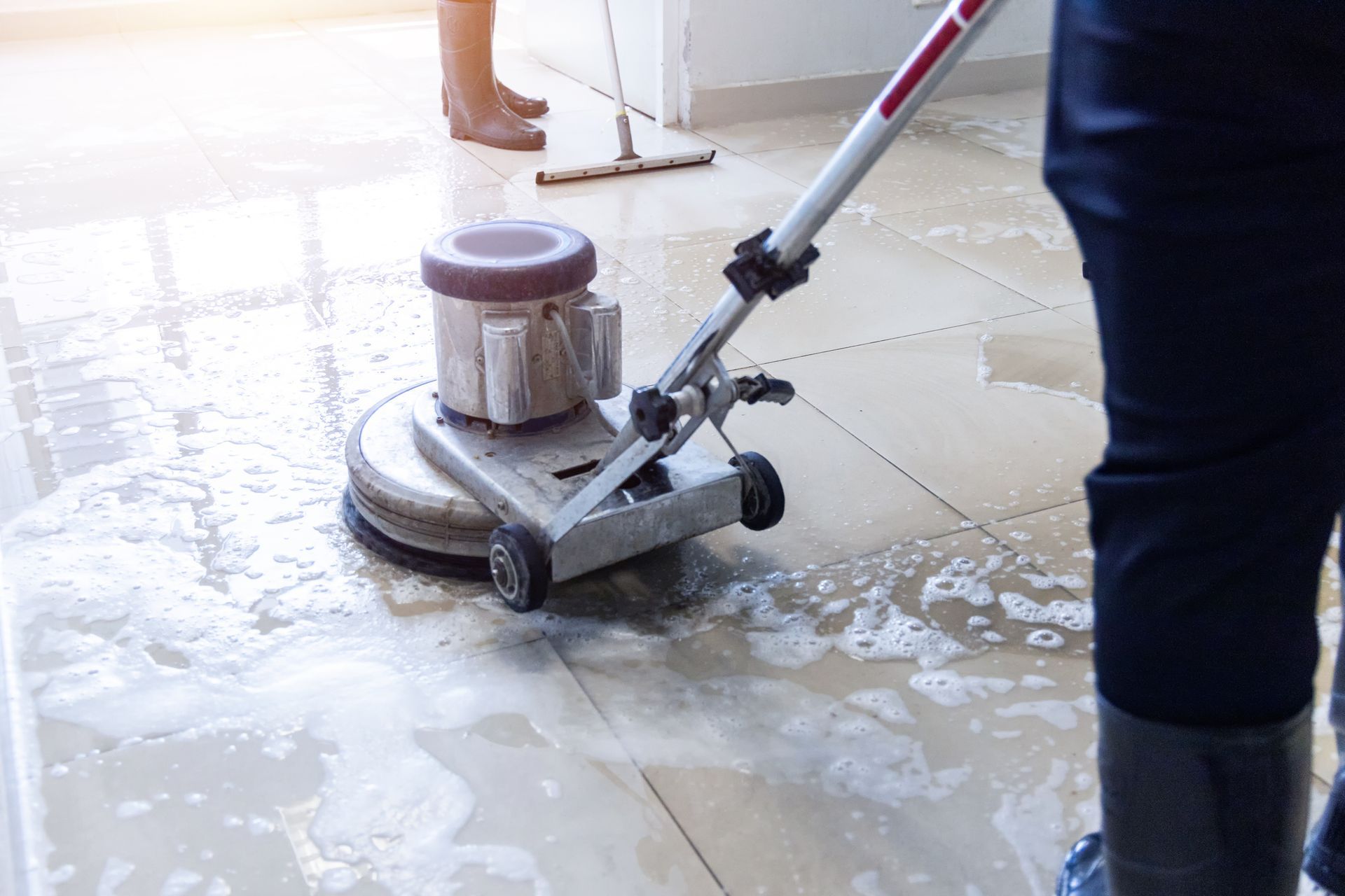 Person cleaning a tiled floor with a floor buffer, leaving wet streaks behind