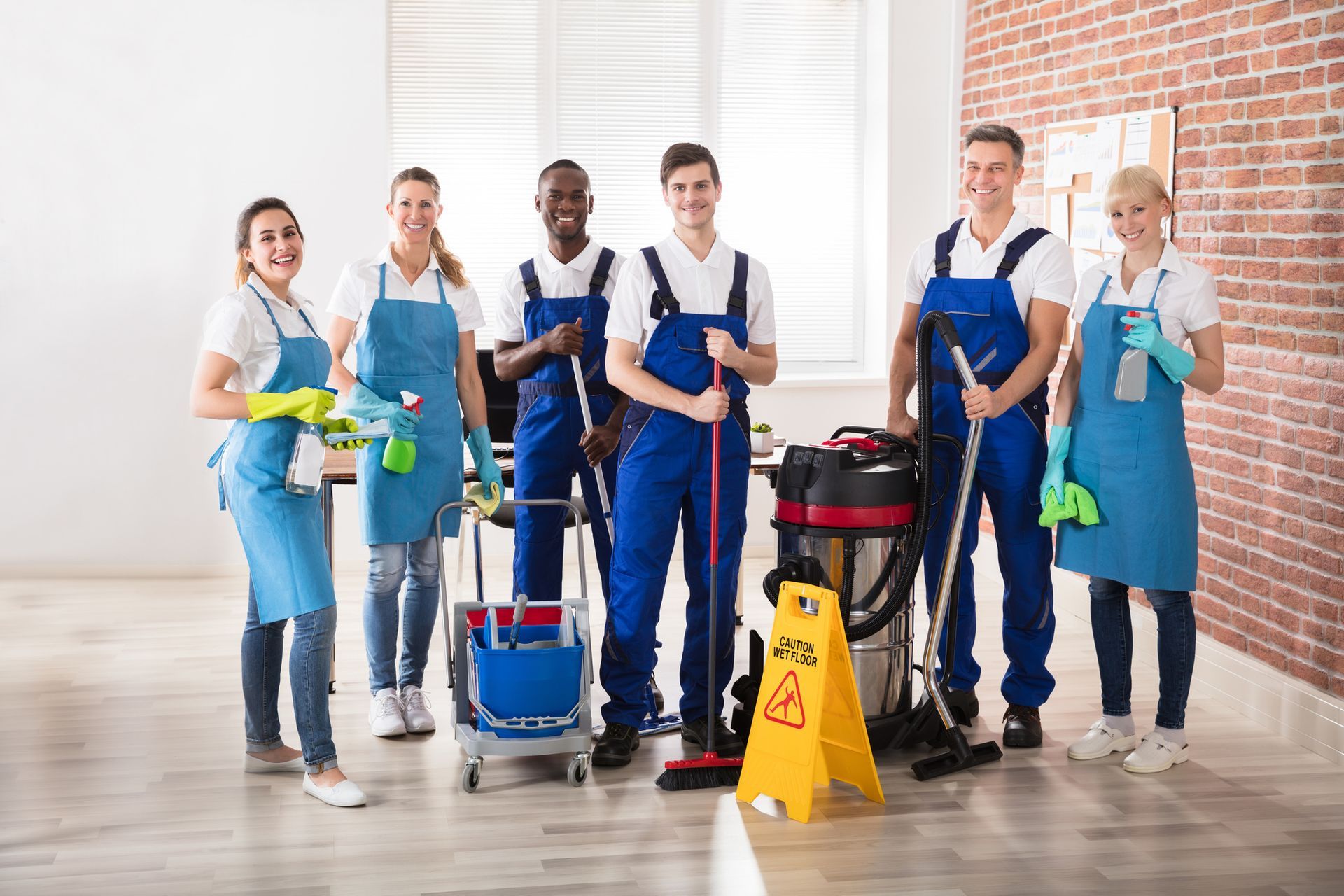 Cleaning crew with mops and supplies in a bright indoor room, standing beside a caution wet floor sign