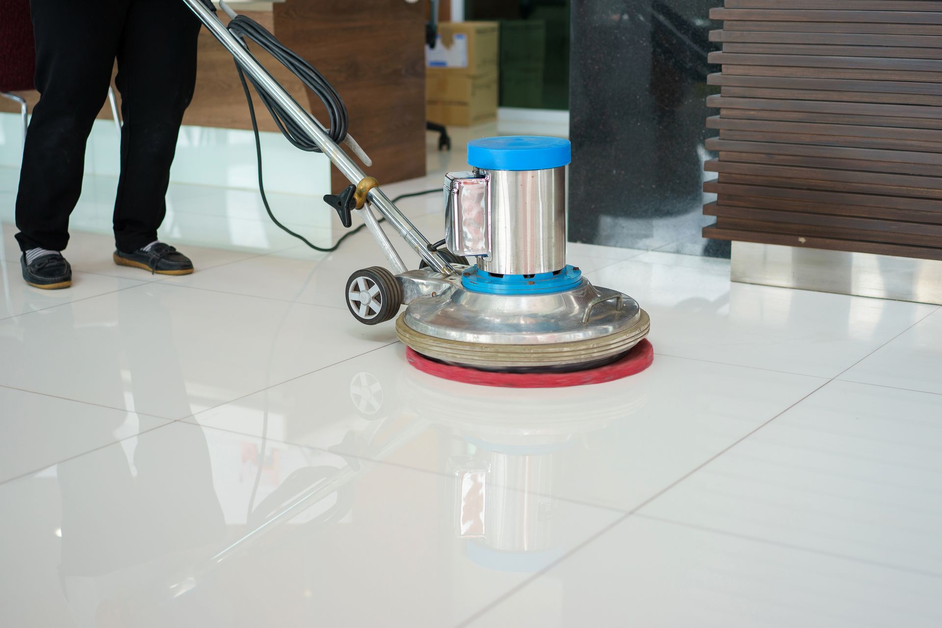 Person operating a floor buffer on a shiny tiled floor indoors