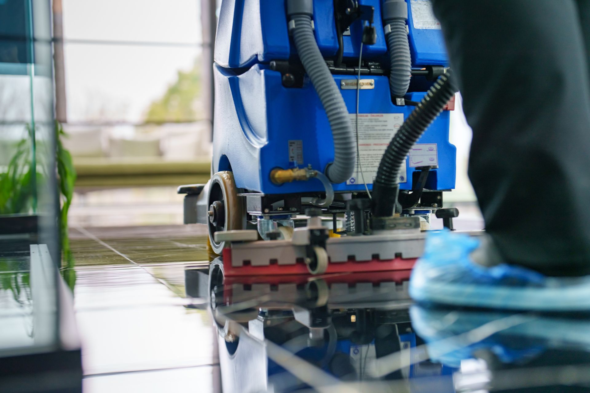 Blue industrial cleaning machine scrubbing a wet tiled floor indoors