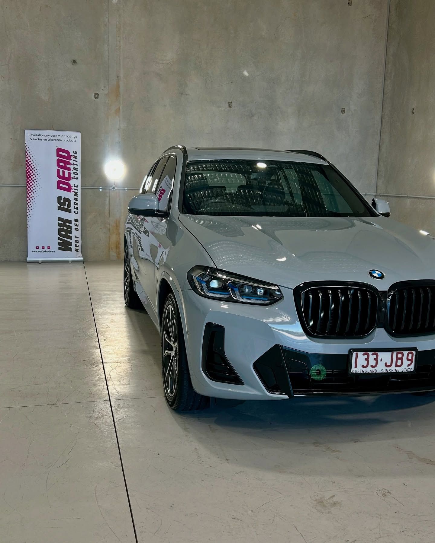 Gray BMW X3 SUV parked in a garage with a banner that reads 