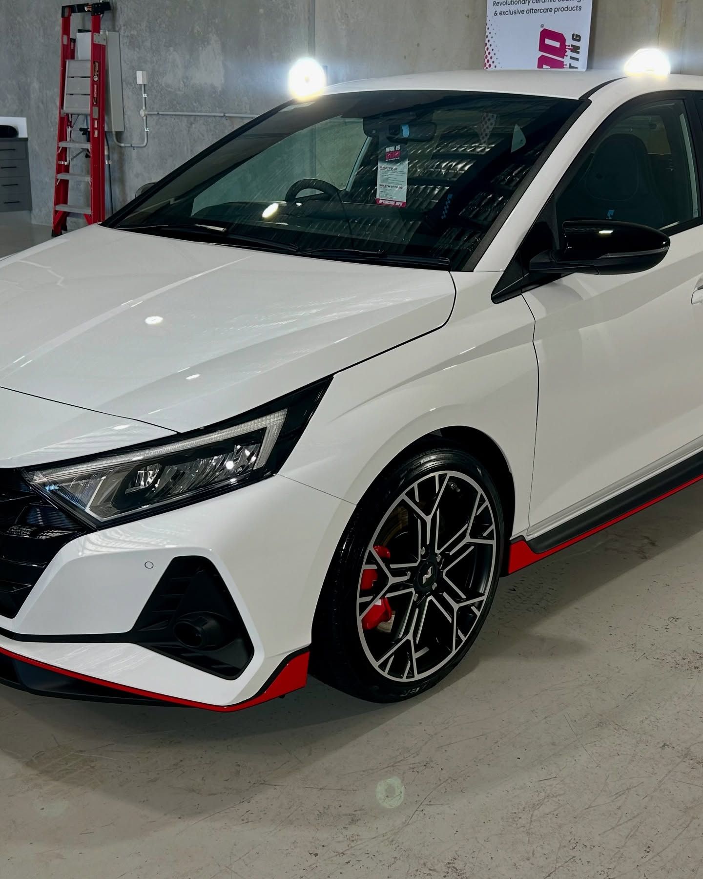 White Hyundai i20 N car with black accents and red trim. Black and red alloy wheels. Parked in a garage — Tim Kratzke Detailing in Pialba, QLD