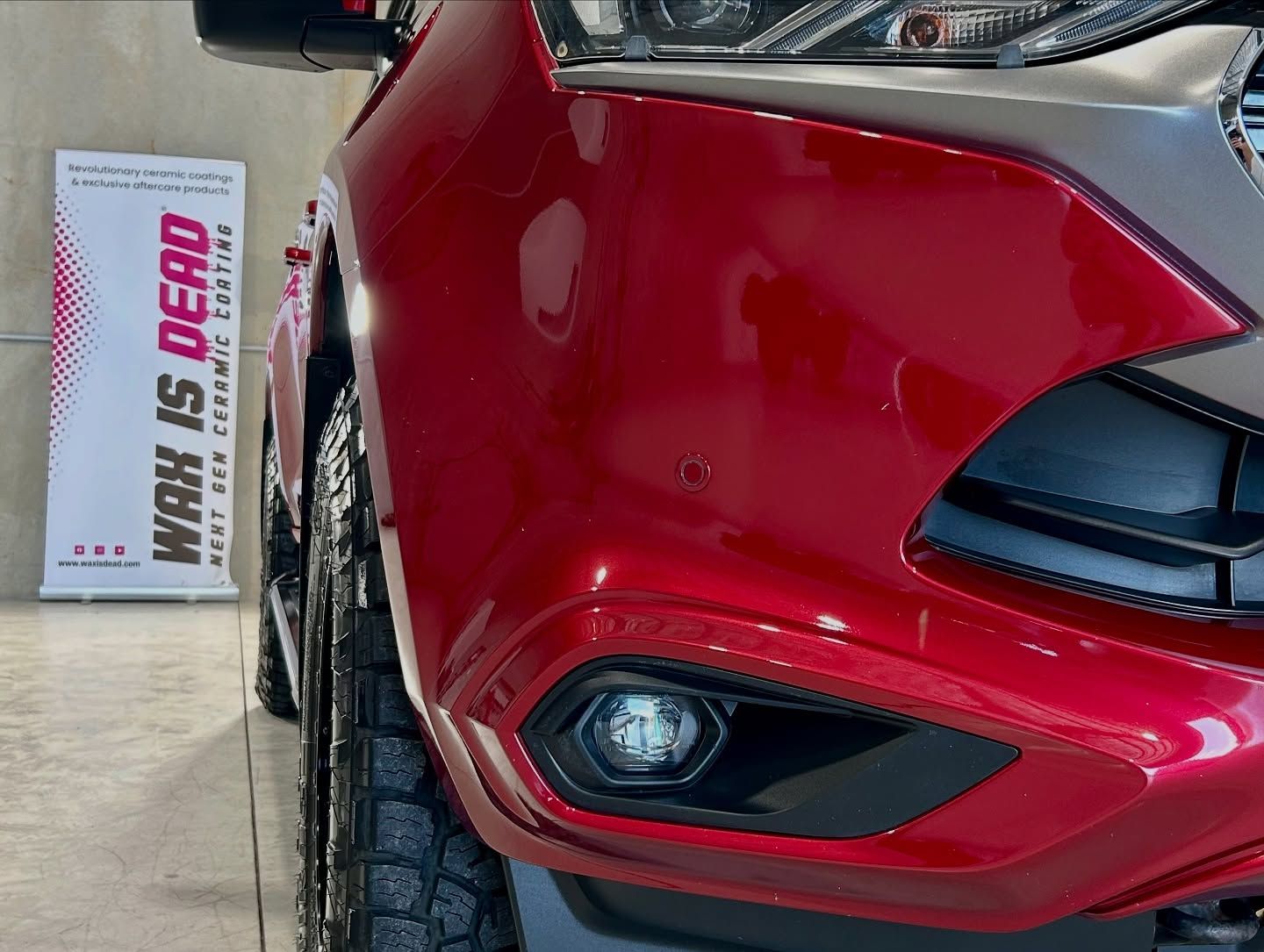 Red car bumper with a fog light, black grill, and a Wax is Dead ceramic coating sign — Tim Kratzke Detailing in Pialba, QLD