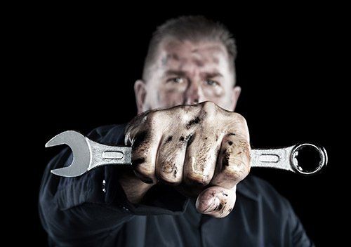 Mechanic holding a wrench toward the camera against a dark background