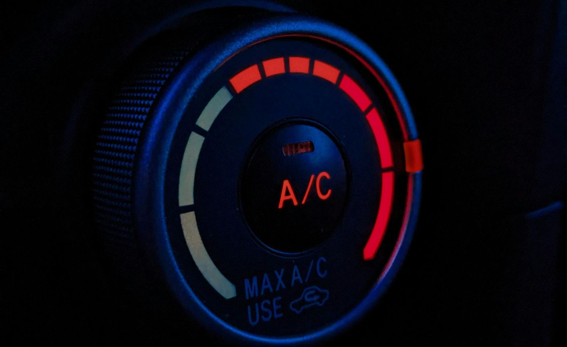 Close-up of car climate control dial set to A/C, glowing red and blue in the dark