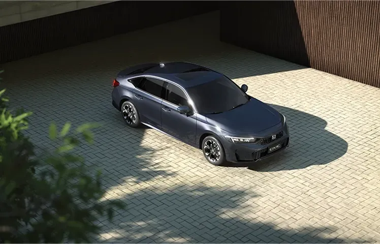 Um sedã cinza escuro estacionado em uma entrada pavimentada em frente a um prédio.