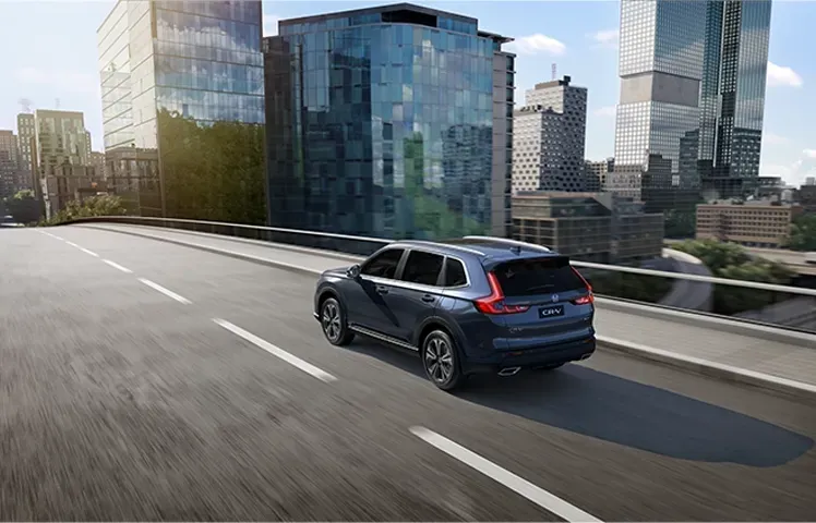 Um SUV azul trafega em uma rodovia elevada da cidade, com modernos edifícios de vidro nas proximidades.