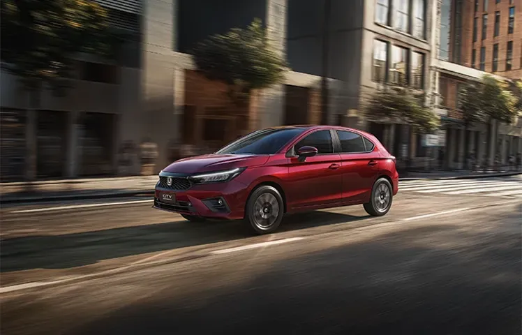 Um hatchback vermelho percorrendo uma rua da cidade, passando por prédios altos.