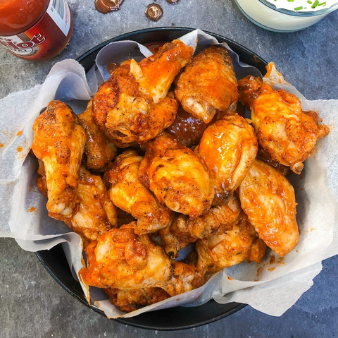 A bowl of chicken wings with a bottle of ketchup in the background.