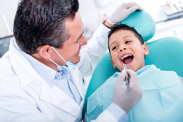 Dentist examining a smiling child in a dental chair with a blue bib and dental tools