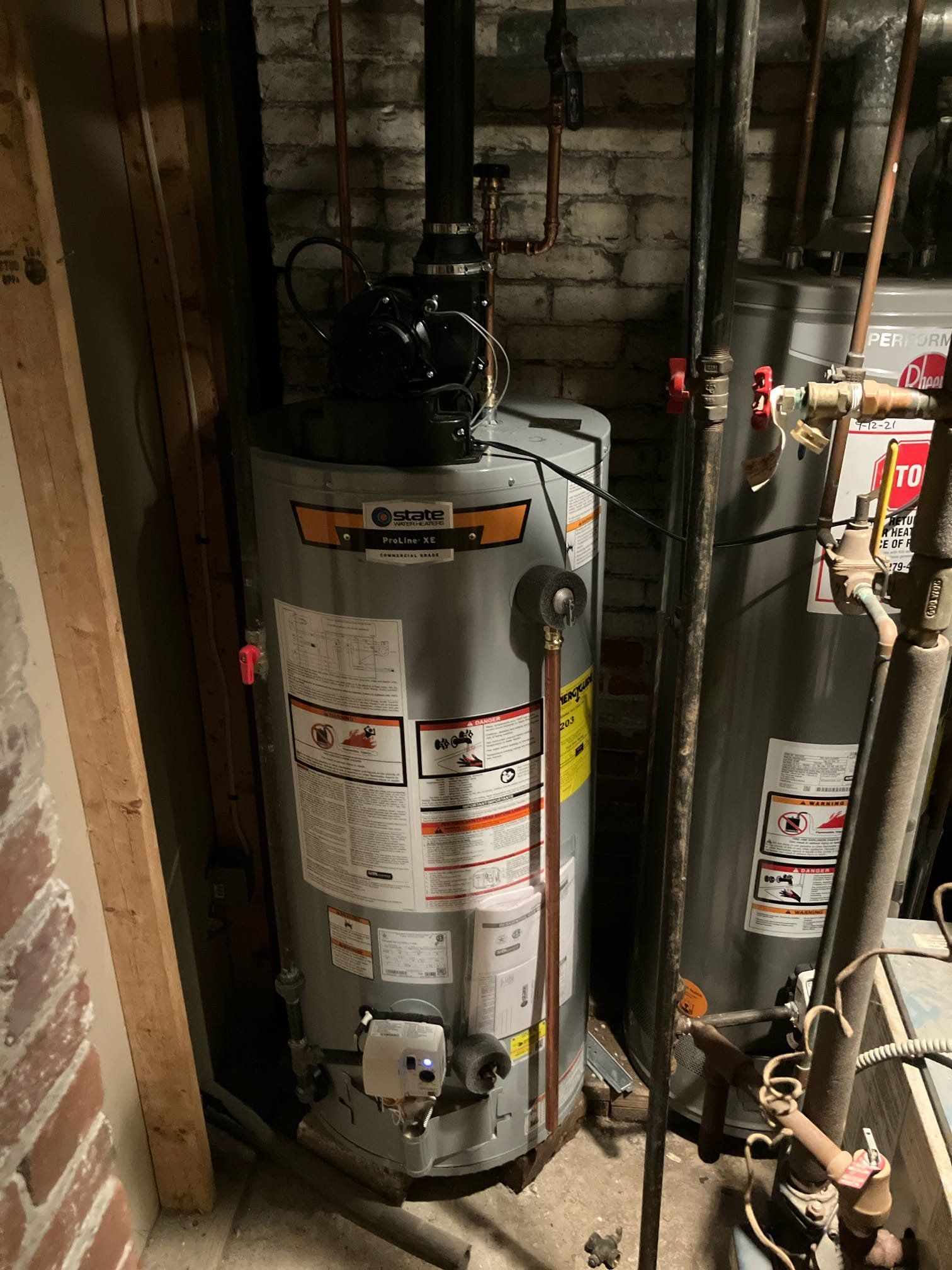 Tall silver water heater in a narrow utility closet with pipes and valves around it