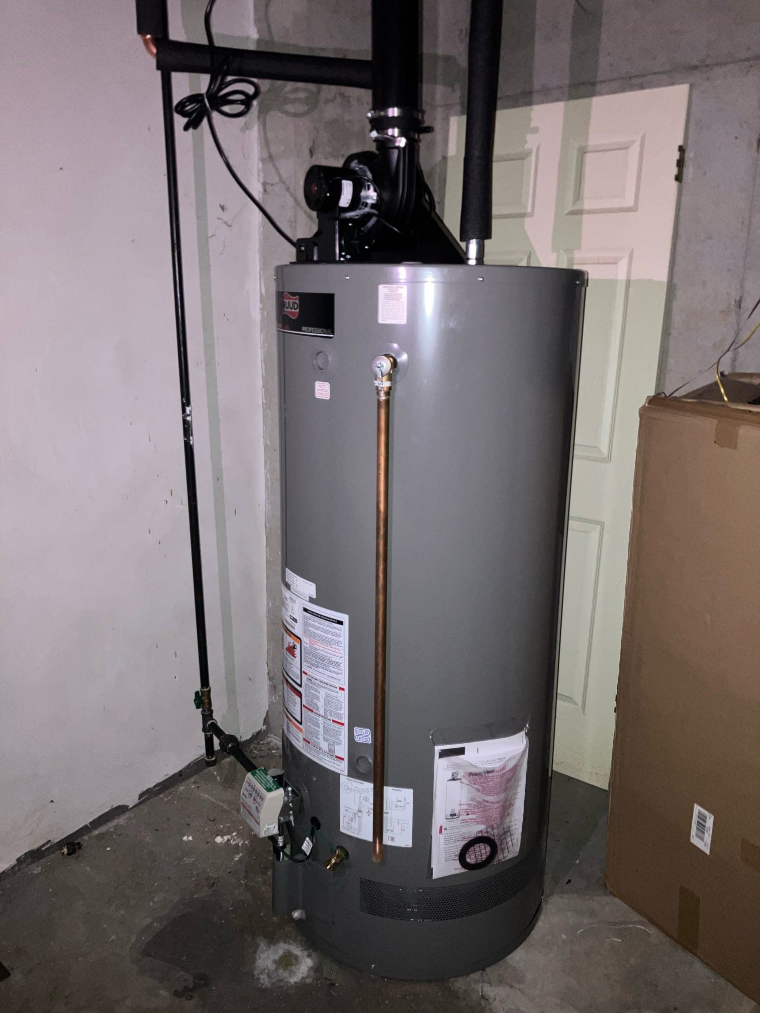 Gray water heater in a basement utility room with pipes and wall wiring.