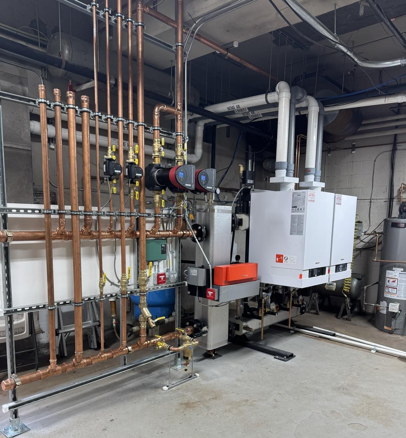 Industrial boiler room with copper pipes, valves, and white HVAC units on a concrete floor