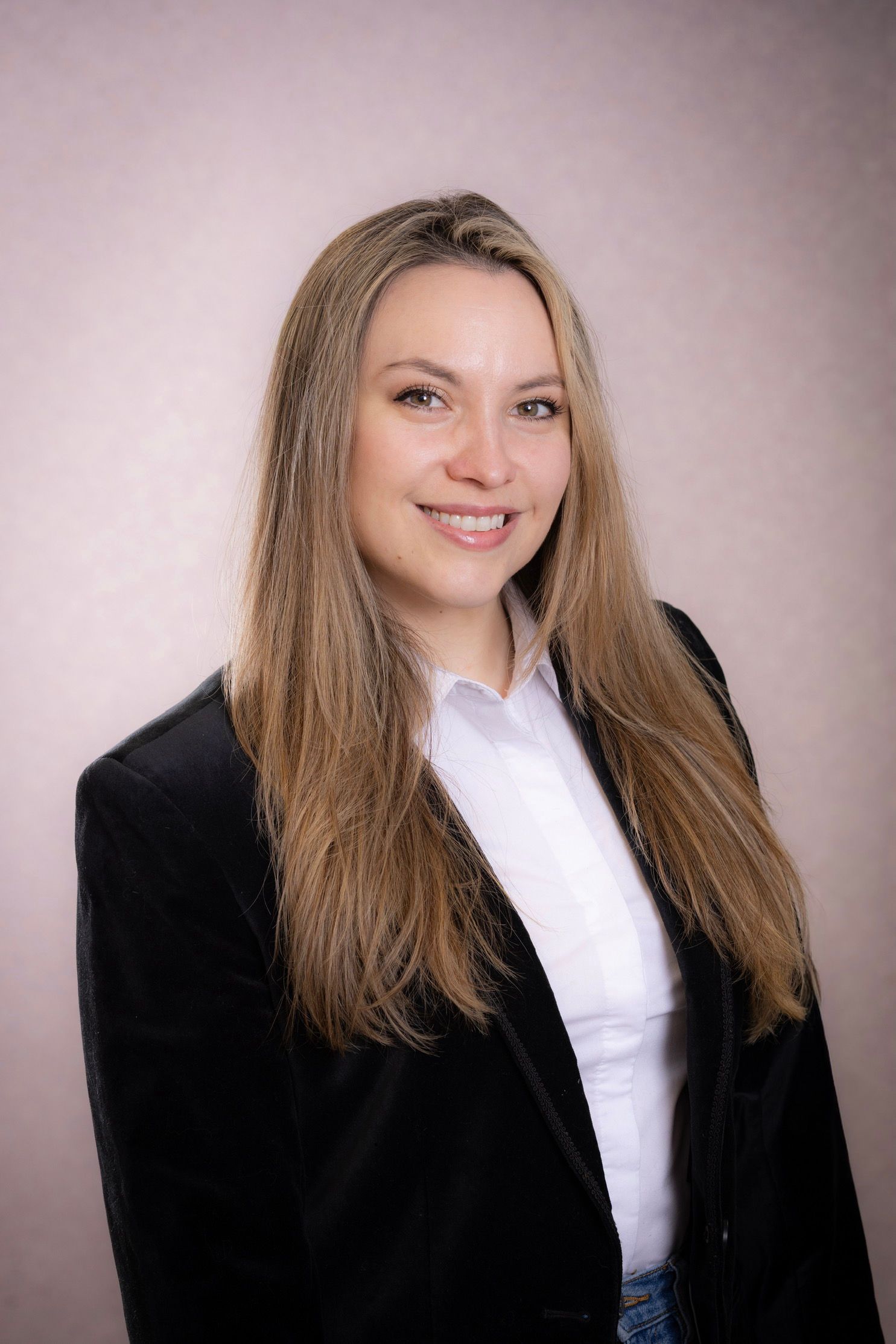 Portrait of a smiling person in a black blazer and white shirt against a soft pink background