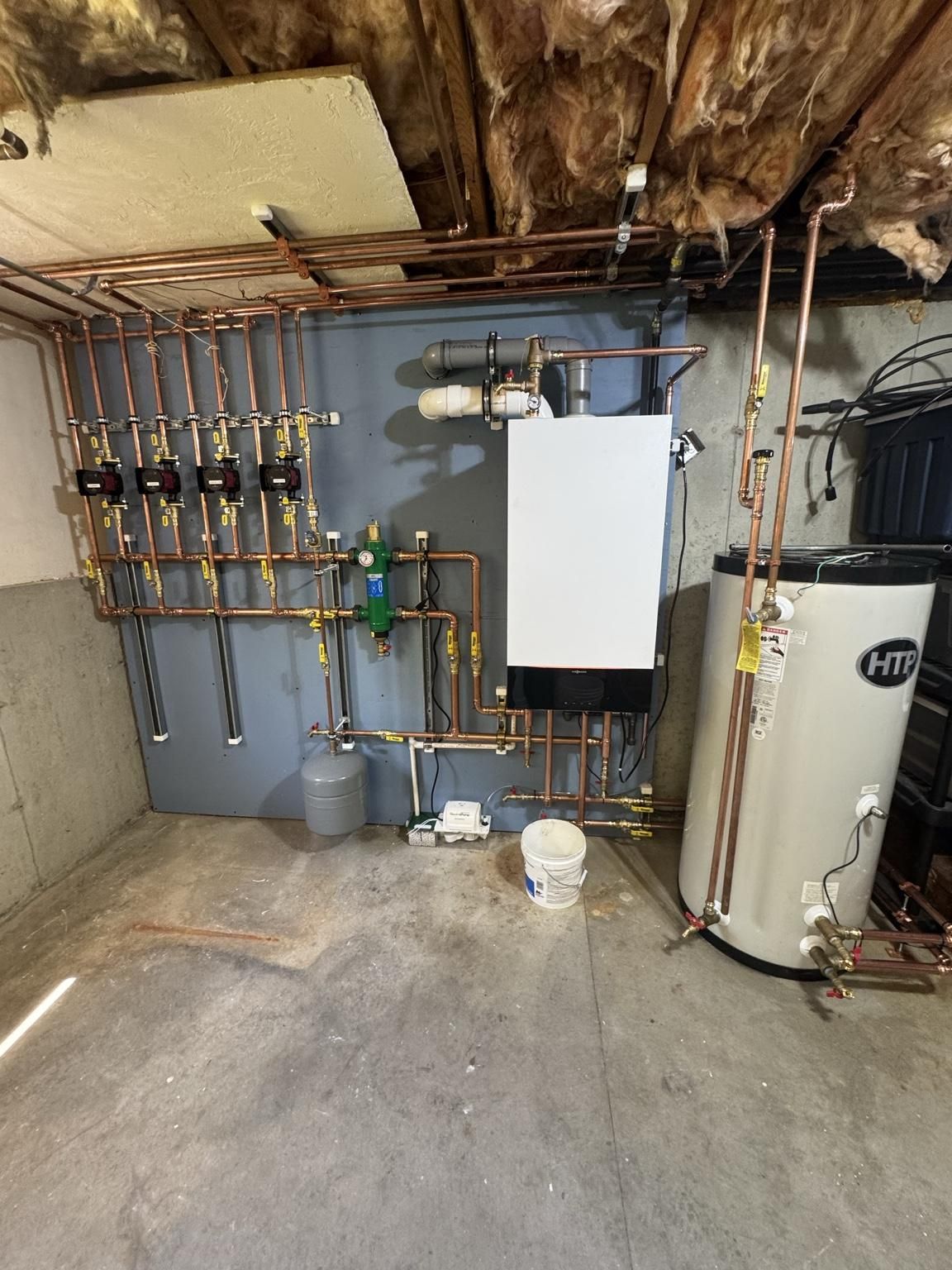 Boiler room with water heater, plumbing manifold, pipes, and utility tanks against a concrete wall
