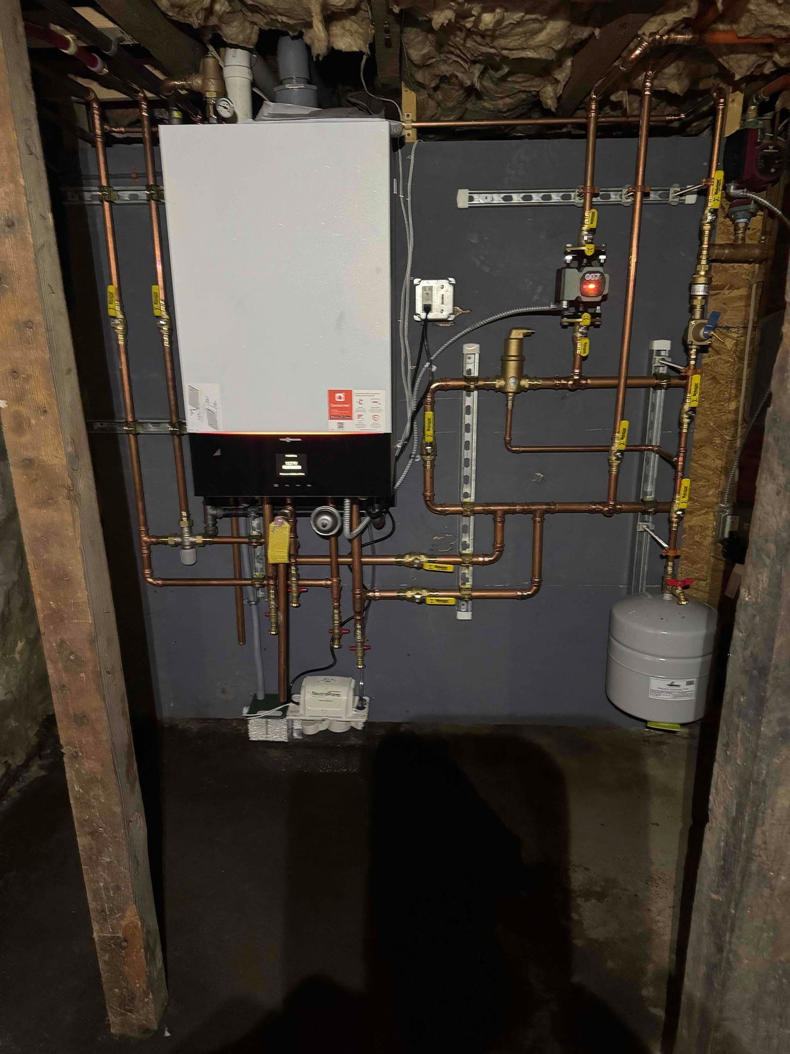 Utility room with a white boiler, exposed copper pipes, and a water tank on a gray wall.