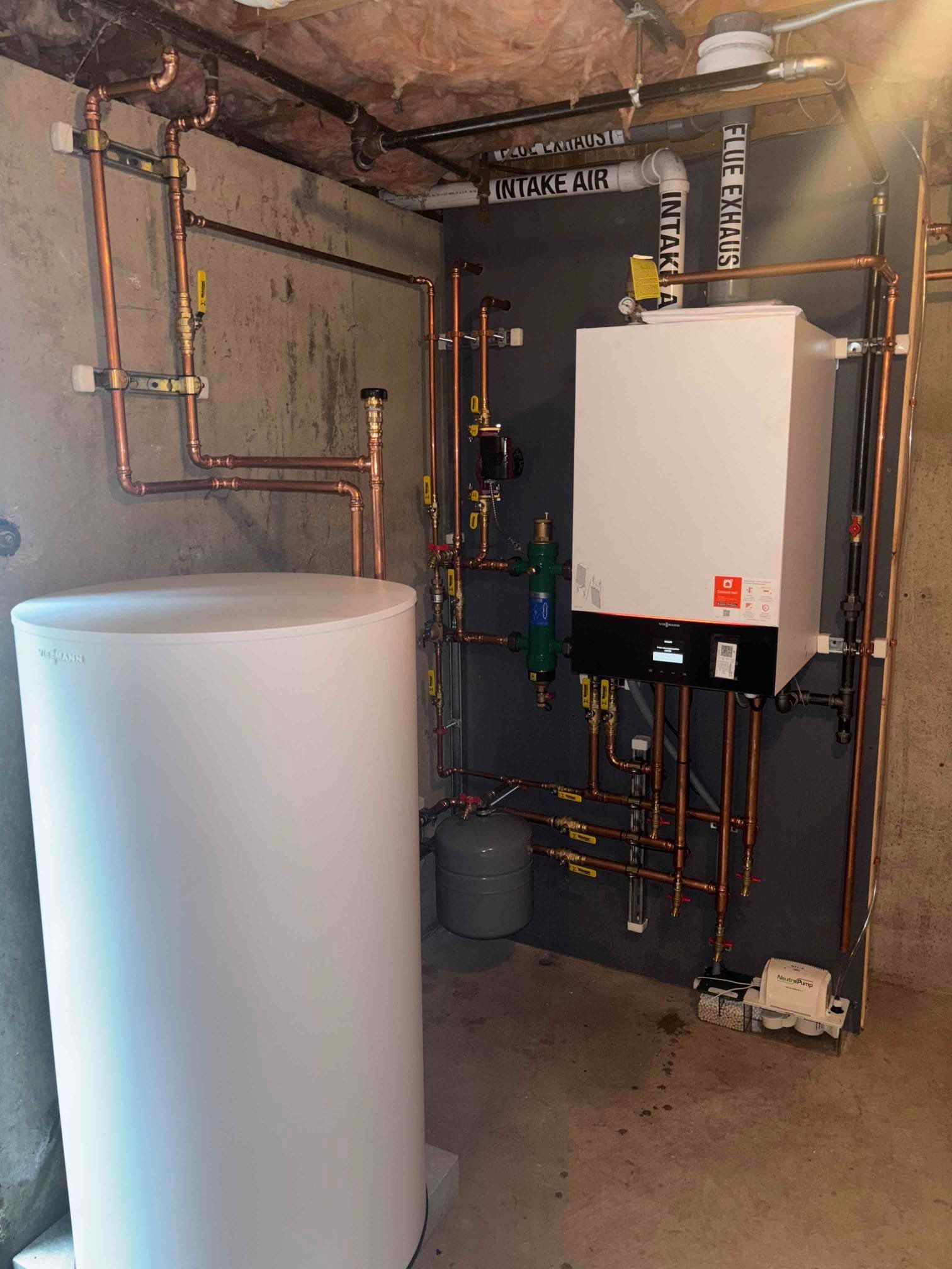 Basement utility room with water heater, boiler, exposed pipes, and concrete floor.