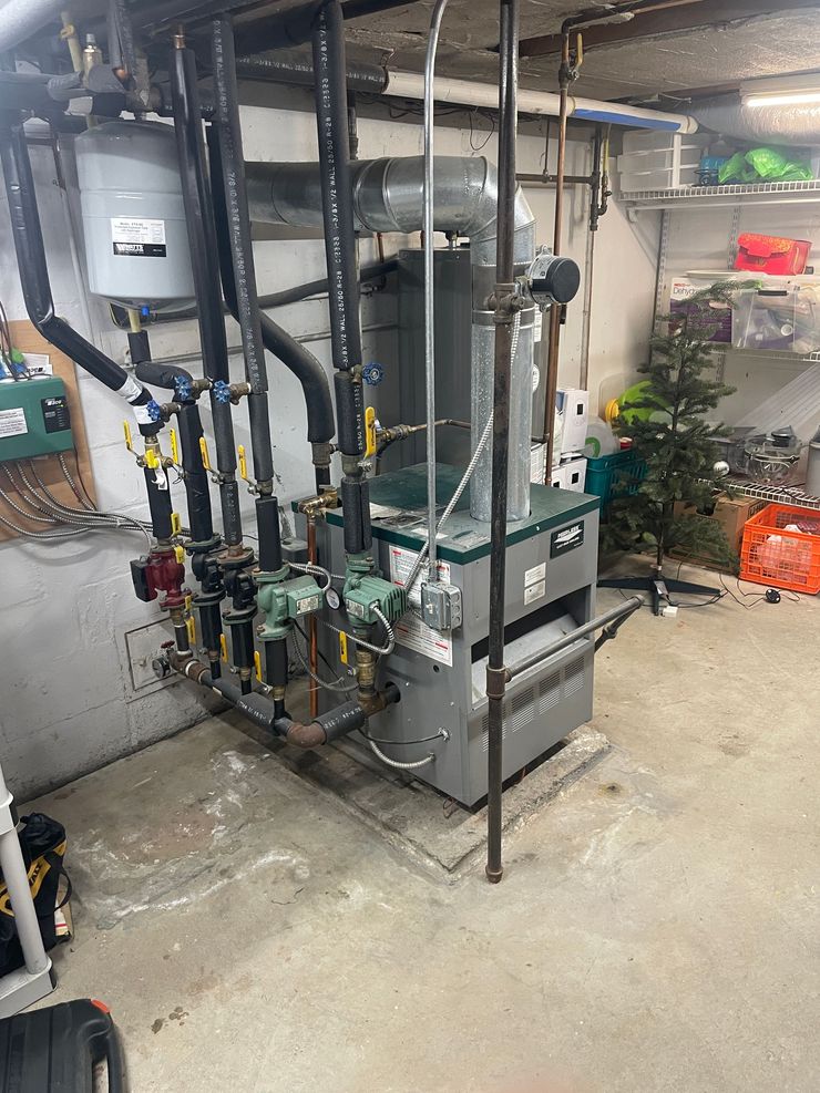 Basement utility room with HVAC equipment, pipes, valves, and storage items along the wall.