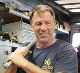 Smiling man in a dark T-shirt standing inside a workshop or vehicle interior
