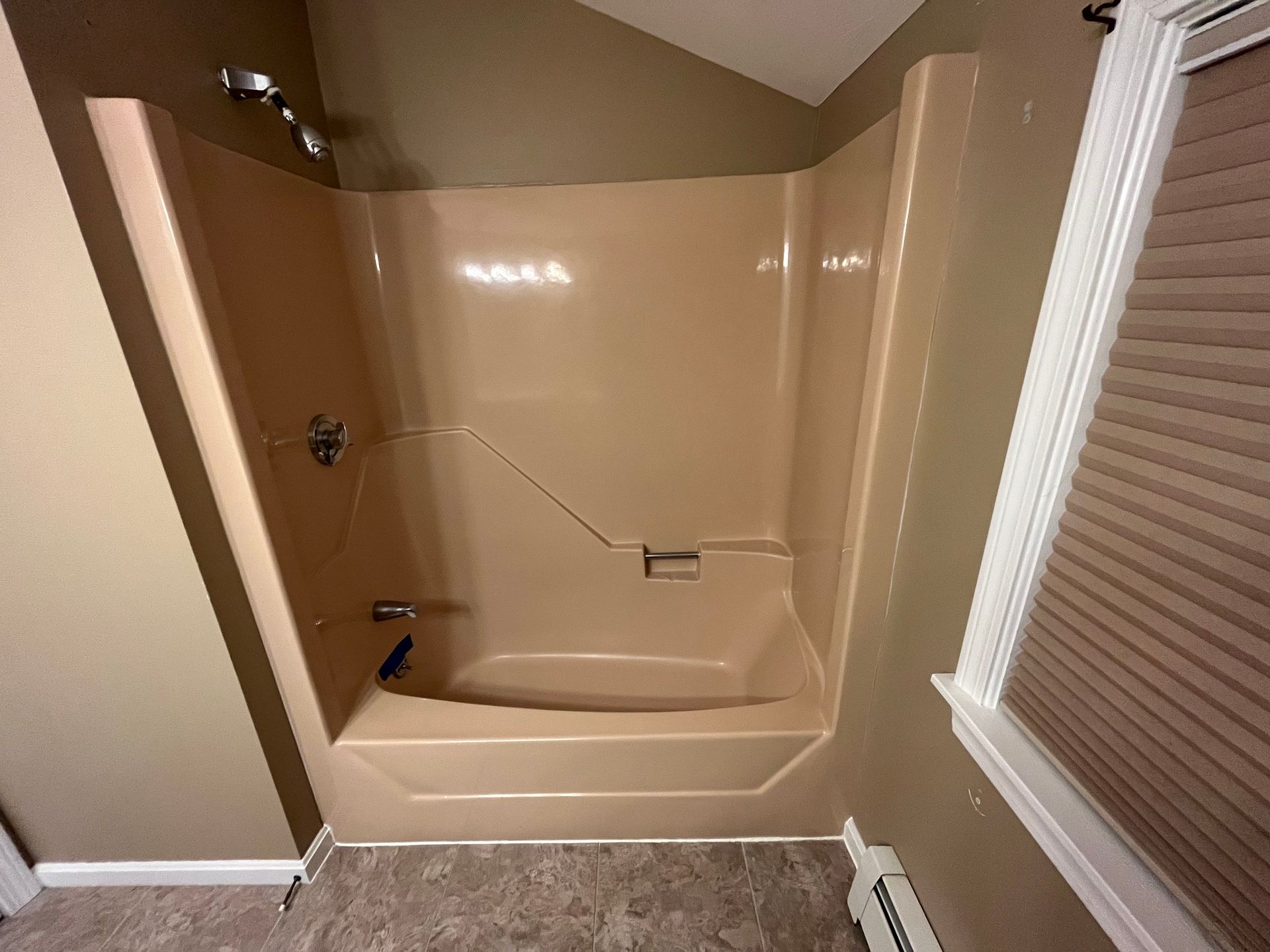 Empty beige shower/tub with glass doors and window blinds beside it