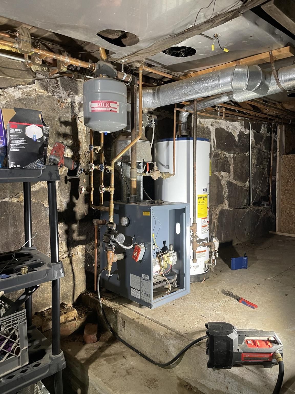 Basement utility room with furnace, water heater, exposed pipes, and tools on the floor.