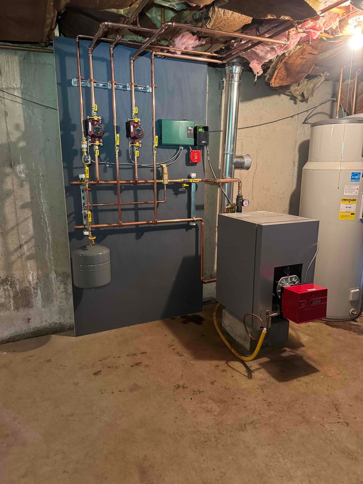 Basement utility room with water heaters, copper pipes, and a furnace on a concrete floor.