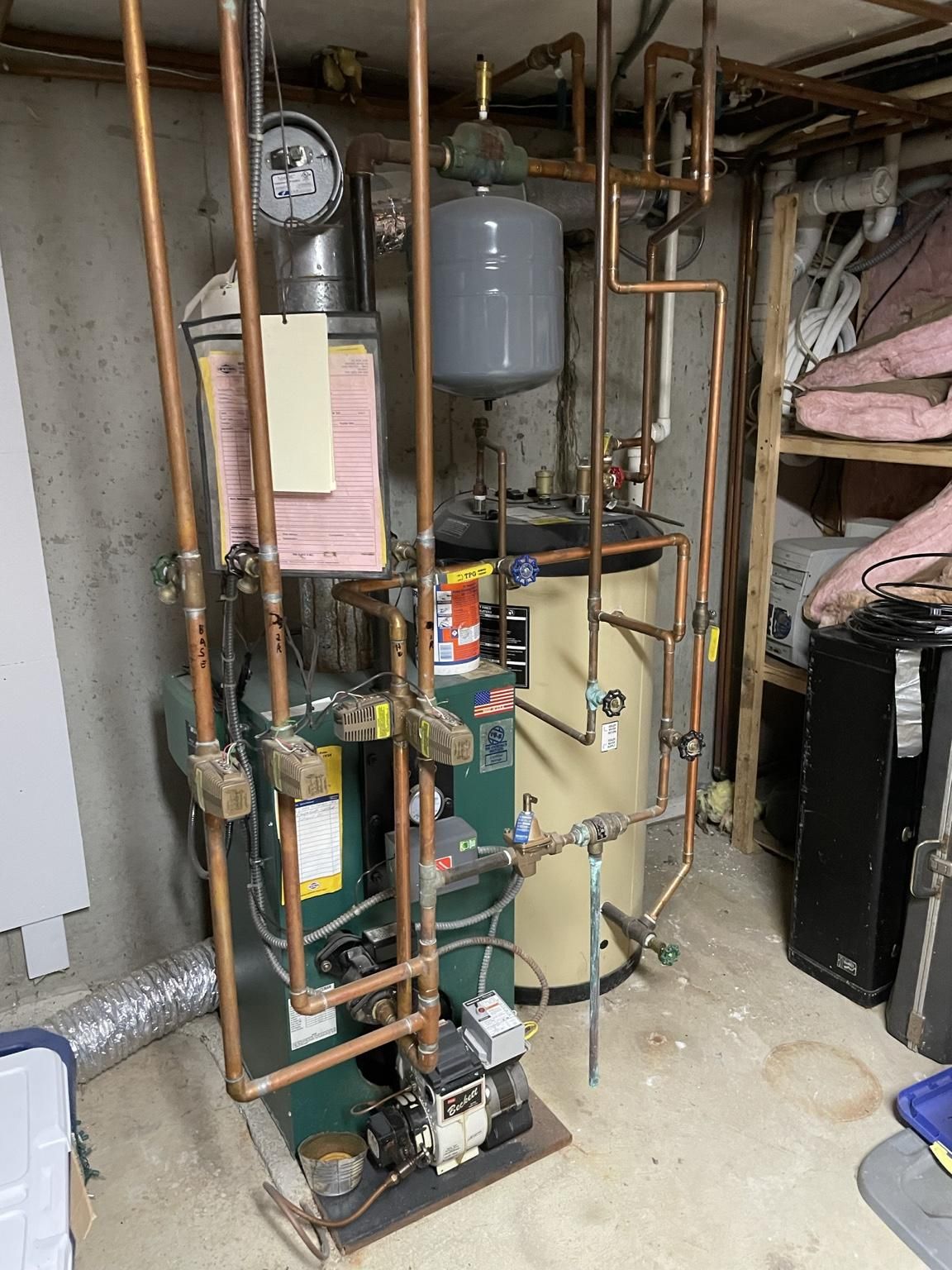 Boiler room with exposed copper pipes, pressure tank, gauges, and utility equipment in a basement.