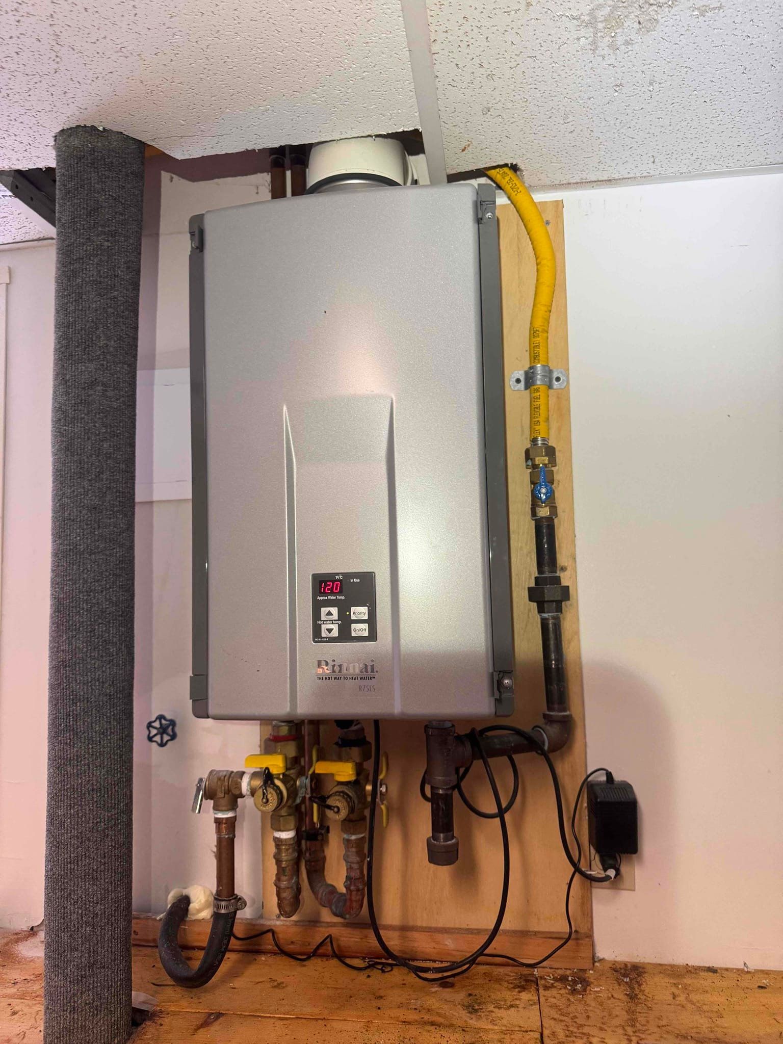 Wall-mounted water heater with yellow gas line and pipes in a utility room.