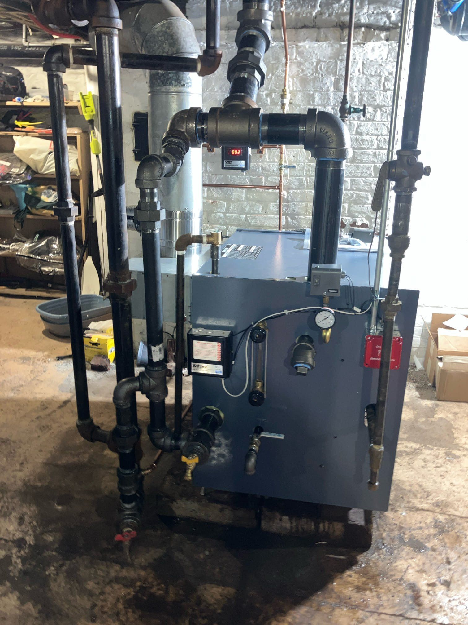 Industrial boiler or heating unit with black pipes and gauges in a basement utility room.