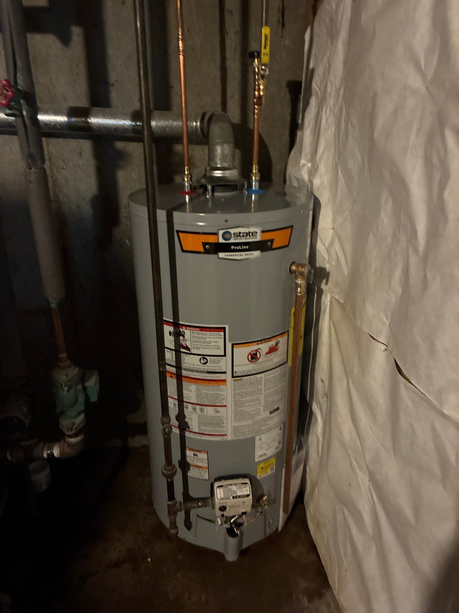 Water heater in a utility room, with pipes and insulation around it.