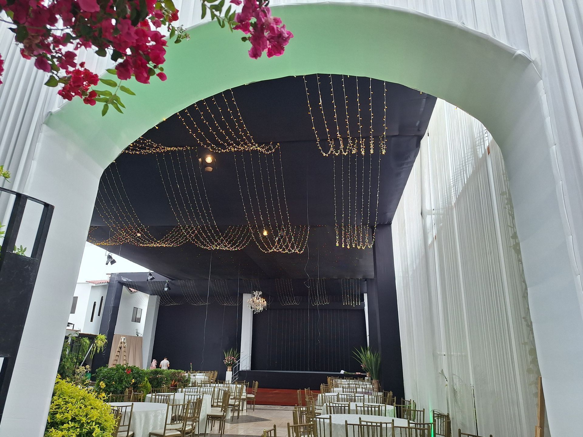 Patio interior decorativo con guirnaldas de luces, arcos blancos y un pequeño escenario en el extremo opuesto.