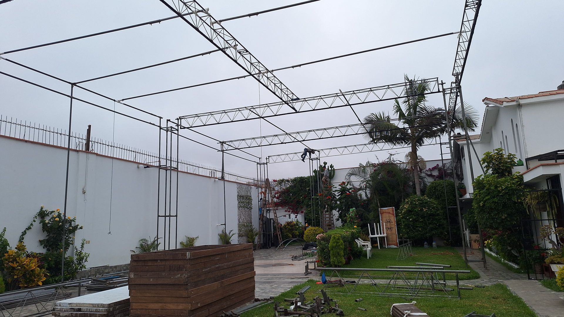 Jardín en la azotea con guirnaldas de luces, plantas en macetas y una jardinera de madera junto a una pared blanca.
