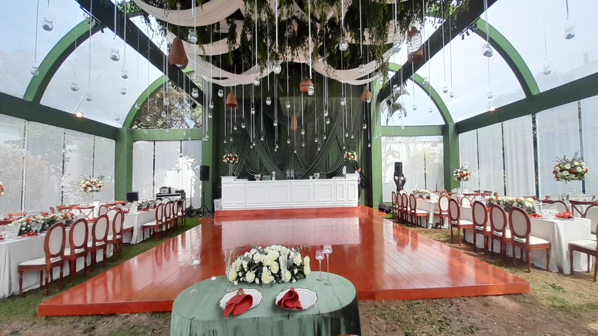 Escenario nupcial interior decorado con alfombra roja, sillas blancas, arreglos florales y vegetación colgante.