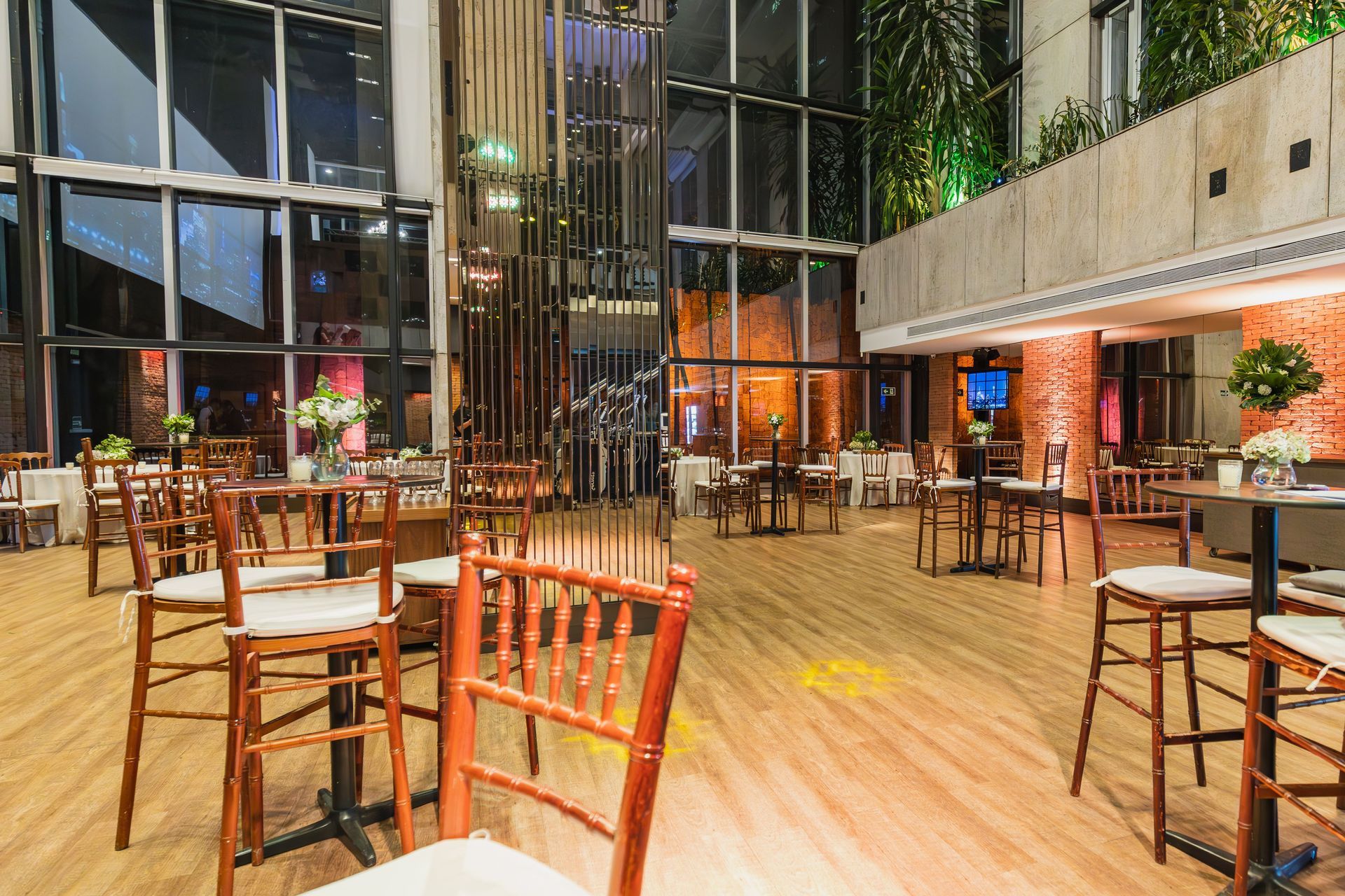 Restaurante moderno de interior con mesas y sillas de madera bajo altas paredes de cristal y una iluminación cálida.