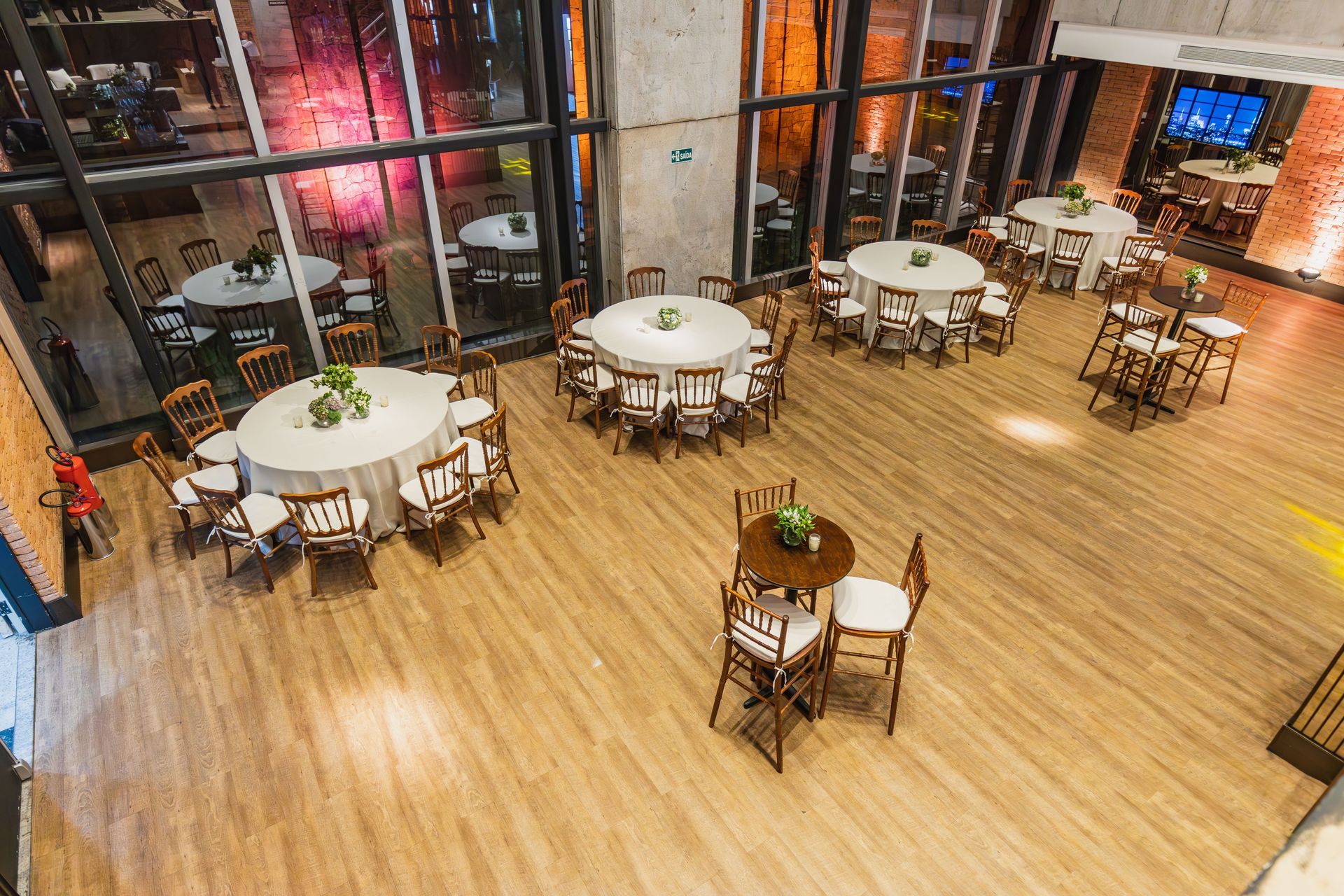 Zona de comedor luminosa del restaurante con mesas redondas, suelo de madera y grandes ventanales por la noche.